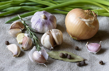 Garlic, garlic slices, onions, rosemary on sackcloth texture background