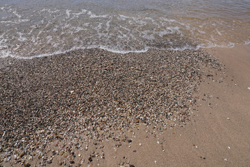 Water washing on shoreline over pebbles on beach on bright sunny day