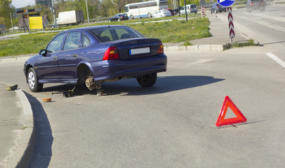 A car on the road with a broken wheel. Emergency sign on the background of the car in repair. 