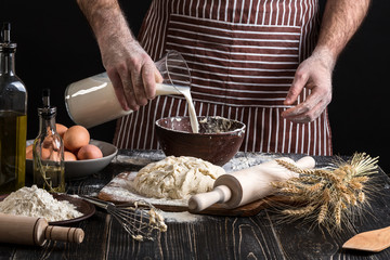 Baker in uniform pouring milk from plastic bottle into bowl. A handful of flour with egg on a...