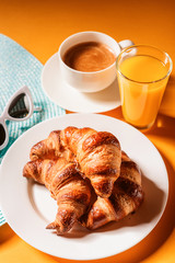 hat, sunglasses croissant with a cup of coffee and a glass of orange juice on a yellow table in the sun