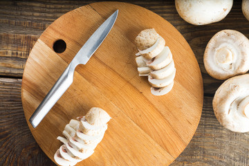 Champignon mushrooms and a knife on a wooden cutting board. Top view