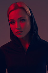 Young pretty woman wearing a black hood and shorts on dark background. Portrait