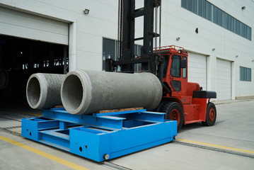 Heavy Forklift loader for warehouse works outdoors with concrete pipes. Industrial production of...