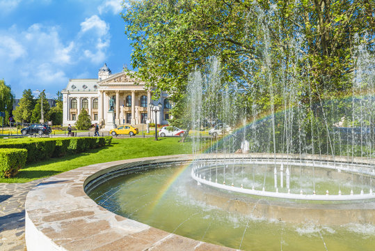 Artesian fountain with rainbow, in background National Opera Theatre of  Iasi, Moldavia, Romania