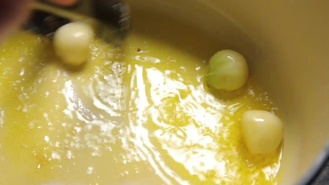A shot of cloves of garlic being put to a hot pot with hot oil.