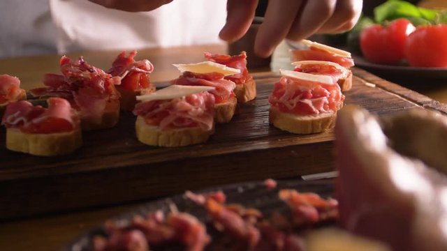 The work of a professional chef for the preparation of traditional Spanish tapas. Unfolding cheese plates on a layer of tomato and bacon.