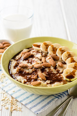 Oatmeal porridge with banana, almonds and chocolate syrup on white wooden background