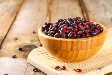 Red raw beans with greens on a wooden table.