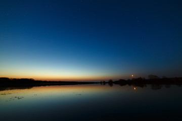 Sky with the stars before dawn. Night landscape with a lake.