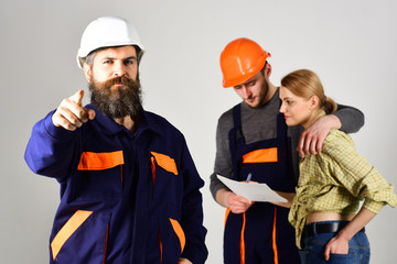 Recruitment concept. Brigade of workers, builders in helmets, repairers and lady discussing contract, grey background. Brigadier hiring workers for repair, sign contract. Bearded man points forward.
