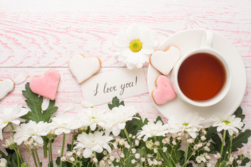 Flowers with tea and cookies in the form of hearts and the inscription love you. Top view on a pink texture with an empty space for inscriptions