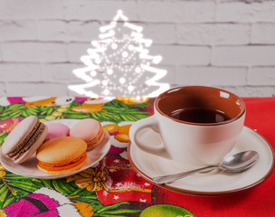 Cup of tea and a plate of macaroons on the table. Background of a gray brick wall. Christmas tree on the wall