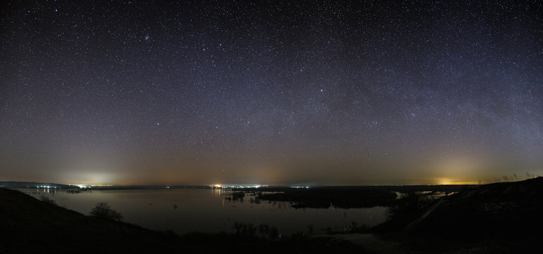 Stars of the Milky Way in the sky before dawn. Night landscape with a lake. Panoramic view of the starry space.