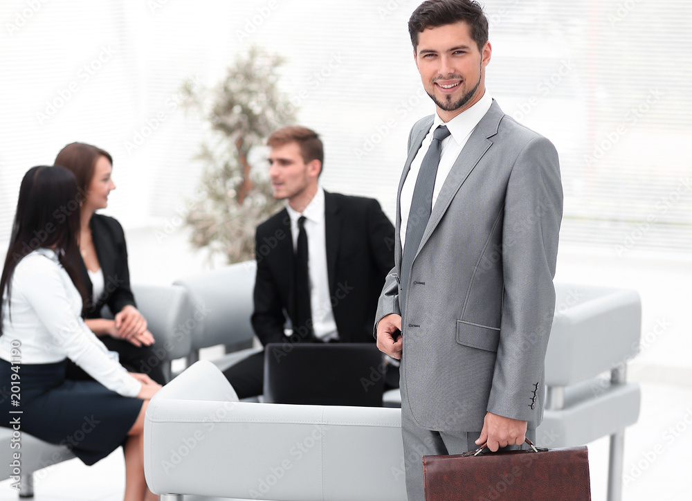 Poster confident businessman with briefcase standing in the lobby of the office.