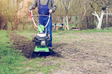 Man working in the spring garden with tiller machine