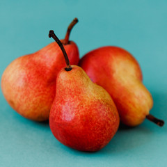 Three bright red williams pears on turquoise background.