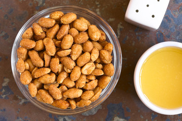 Peanuts with honey and salt in glass bowl, salt and honey on the side. Photographed overhead on slate with natural light
