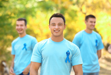 Young man in t-shirt with blue ribbon outdoors. Prostate cancer awareness concept