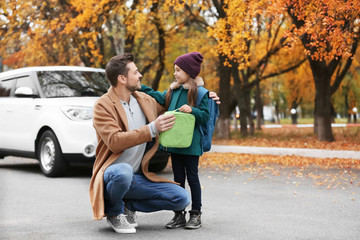 Young man giving lunch bag to his daughter before school