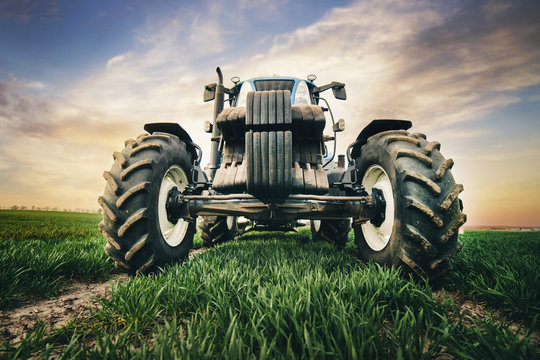 Fototapeta professional tractor with big tires is moving along the road in the field in the spring