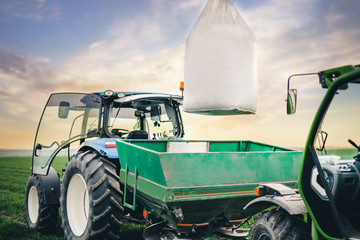 driver puts a sack of fertilizers on a square tractor trailer in the field in the spring