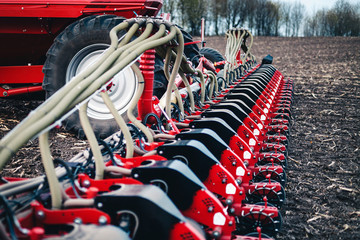 sowing equipment stands on the ground against a tractor background in a field in the spring