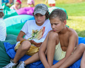 background. two boy friends sit in a green park on a blue soft sofa
