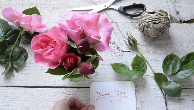 Top view of female decorator leaving "Thank you" card, arranging roses on the wooden table, Concepts - fiorist, occupation, hobby, small business  