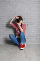 Young female photographer with camera near brick wall