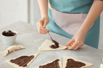 Woman preparing tasty croissants with chocolate paste on table, closeup