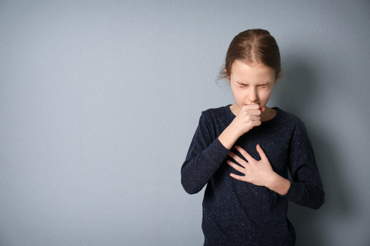 Girl coughing on grey background