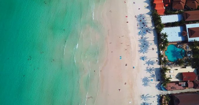 AERIAL 4K: Tropical beach video loop showing seamless never ending footage, overhead view of green foaming waves crushing against the sandy coast line, people enjoy summer  near resorts and hotel line