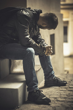 Young Depressed Man Sitting In The Dark Alleyway, Feeling Sadness And Pain