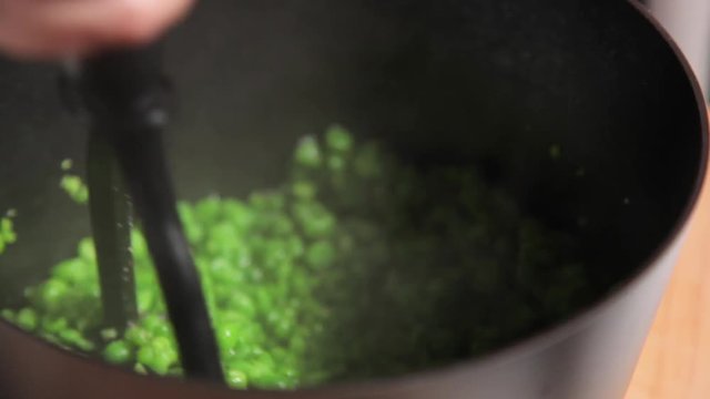 A close up shot of a woman smashing green pease in a pot.