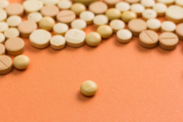 Heap of assorted beige capsules on orange table. One pill is apart, isolated.