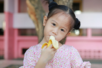 Adorable Asian kid girl eating banana.