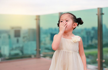 Cute little child girl in dress with using hands close her mouth at the rooftop of building.