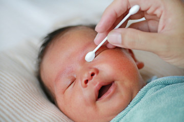 Mother use cotton bud to clean baby eyes.