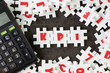 KPI, Key Point Indicator concept, white puzzle jigsaw alphabet combine word KPI at the center with calculator on dark black cement floor, business success target and measurement