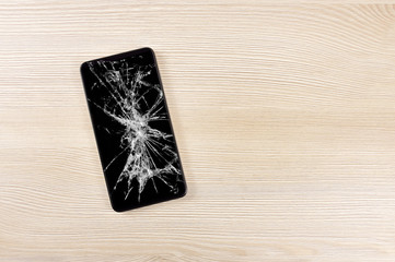 Modern mobile phone with broken screen on wooden background and copy space