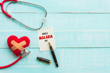 World MALARIA day April 25, Healthcare and medical concept. Stethoscope, red and black heart, thermometer and yellow Pill on blue Pastel wooden table background texture.