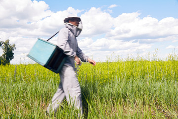 Full length portrait of young beekeeper in protective workwear carrying tools walking in sunny green meadow, copy space