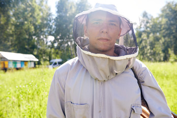 Portrait of beekeeper in protective mask posing looking at camera confidently standing in sunny green meadow, copy space