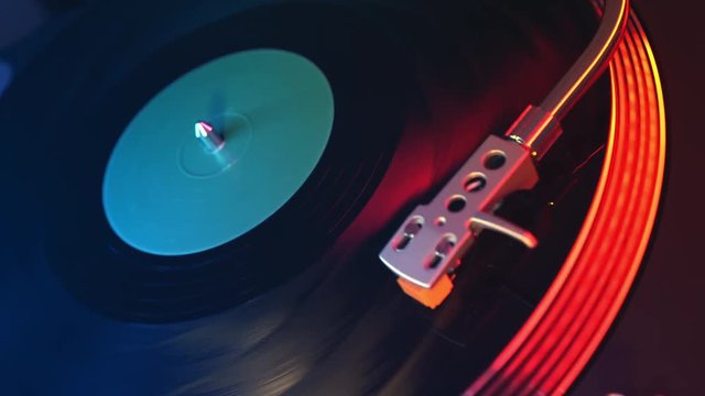 Defocus in focus player vinyl records turntable closeup on a background of red and blue lights. The needle slides smoothly on a spinning black vinyl record
