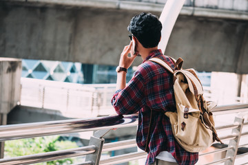 Casual Young asian man with backpack talking on mobile phone in the city.