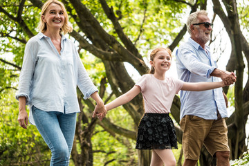 Happy family having fun together in the garden. Father, mother and daughter holding hands and walking in a park. Lifestyle concept