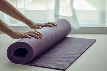 Hands of woman folding purple yoga mat or fitness mat after working out.