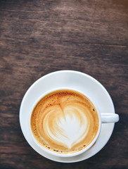Coffee with heart-shaped cream, white cup on the wood table.