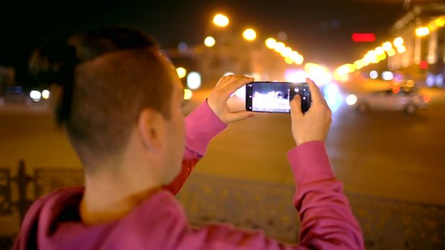 Man taking photo with camera phone at night city. Young casual man taking picture with camera phone outside. 4 k Young man with smartphone in night city.